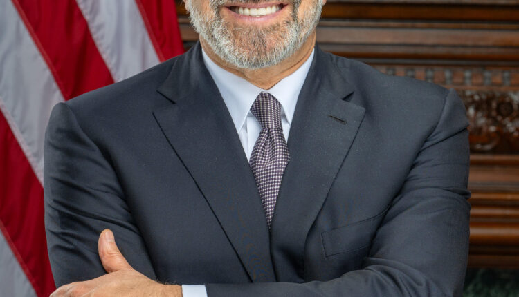 Portrait of U.S. Commerce Secretary Howard Lutnick in a suit standing before an American flag.